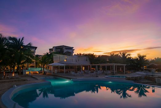 Beautiful hotel with a swimming pool at dawn in the golden rays of the sun. Reflection in the blue water of pink clouds.