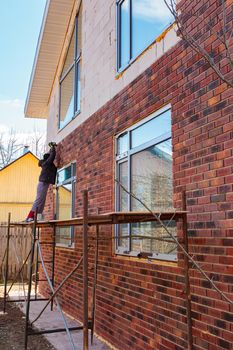 A man works with a drill, attaches thermal panels made of clinker to the facade of the house. Clinker bricks and tiles in brown color