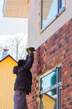 A man works with a drill, attaches thermal panels made of clinker to the facade of the house. Clinker bricks and tiles in brown color