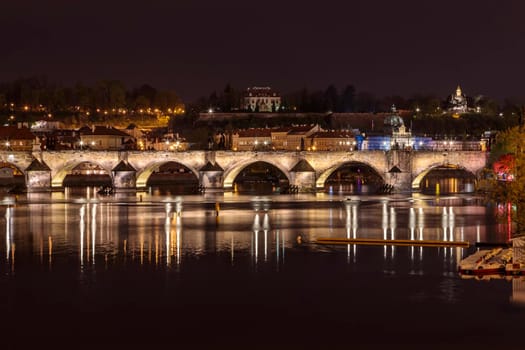 Charles Bridge in Prague in the evening with colorful lights from lanterns. In the river the reflection of the evening illuminations.