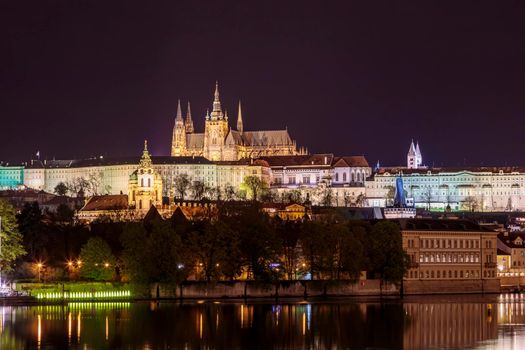 Charles Bridge in Prague in the evening with colorful lights from lanterns. In the river the reflection of the evening illuminations.