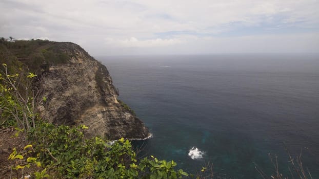 Cliff with waves crashing against rocky shore, Nusa Penida, Indonesia. Rocky coast and ocean with waves and rocky cliff. Travel concept.