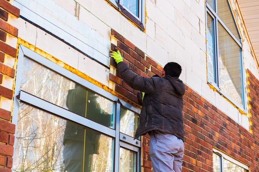 A man works with a drill, attaches thermal panels made of clinker to the facade of the house. Clinker bricks and tiles in brown color