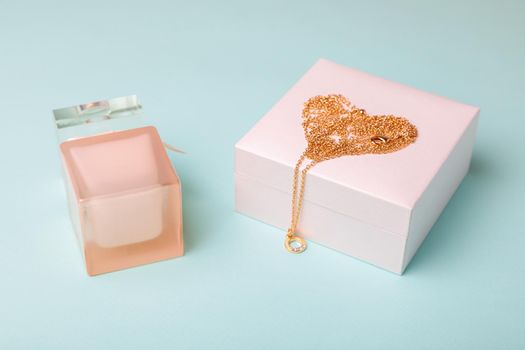 A gift for Valentine's Day. Perfume and a box with a gold chain on a blue background. Chain in the shape of a heart.