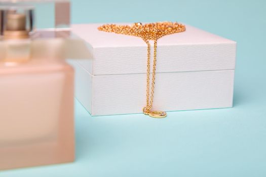 A gift for Valentine's Day. Perfume and a box with a gold chain on a blue background. Chain in the shape of a heart.