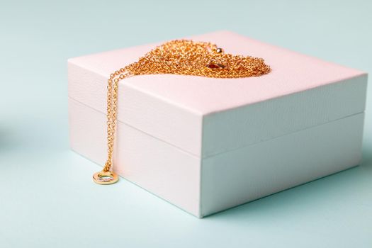 A gift for Valentine's Day. Perfume and a box with a gold chain on a blue background. Chain in the shape of a heart.