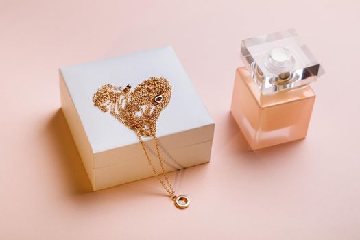 A gift for Valentine's Day. Perfume and a box with a gold chain on a pink background.