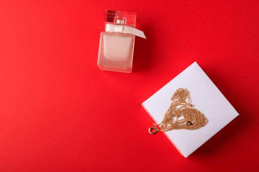 A gift for Valentine's Day. Perfume and a box with a gold chain on a red background.