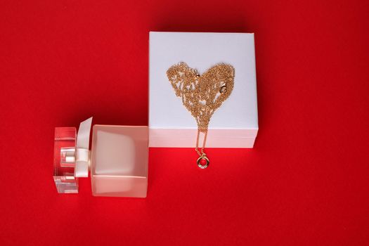A gift for Valentine's Day. Perfume and a box with a gold chain on a red background.