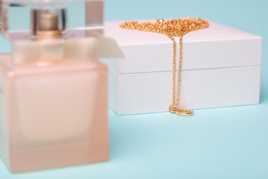 A gift for Valentine's Day. Perfume and a box with a gold chain on a blue background. Chain in the shape of a heart.
