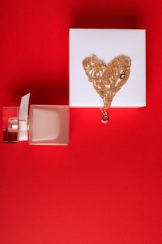 A gift for Valentine's Day. Perfume and a box with a gold chain on a red background.