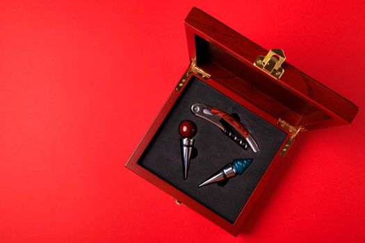 Gift set of corkscrew and removable lids. Wine corks and bottle openers in a wooden box on a red background.