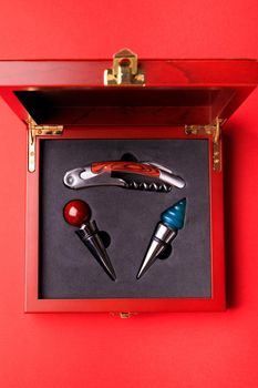 Gift set of corkscrew and removable lids. Wine corks and bottle openers in a wooden box on a red background.