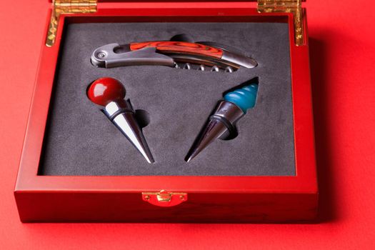 Gift set of corkscrew and removable lids. Wine corks and bottle openers in a wooden box on a red background.