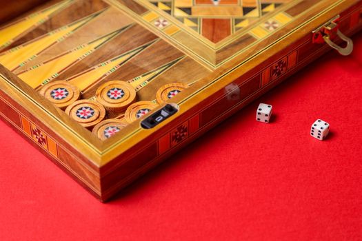 An entertaining game of backgammon on a red background. Checkers, cubes, handmade board