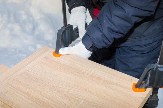 The worker secures the glued chipboards with two clamps. Winter, close-up, outdoor work.