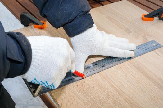 A man, a worker, marks it with a square and a pencil on a chipboard board. Draws a line.