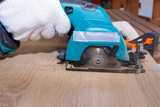 A male worker cuts a wooden panel attached to a workbench with clamps using a circular disc on a battery.