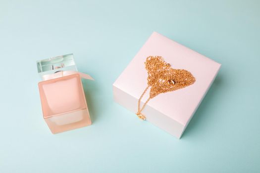 A gift for Valentine's Day. Perfume and a box with a gold chain on a blue background. Chain in the shape of a heart.
