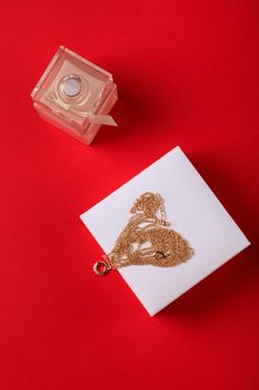 A gift for Valentine's Day. Perfume and a box with a gold chain on a red background.