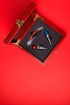 Gift set of corkscrew and removable lids. Wine corks and bottle openers in a wooden box on a red background.