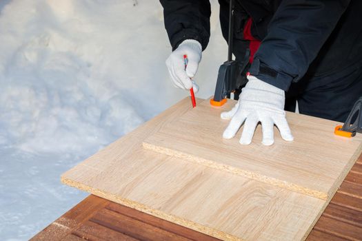 A man, a worker, marks it with a square and a pencil on a chipboard board. Draws a line.