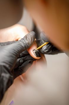 In a beauty salon, the master does a manicure, applies a pattern to the nail with a brush, black varnish with a golden pattern.