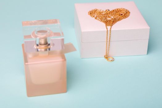 A gift for Valentine's Day. Perfume and a box with a gold chain on a blue background. Chain in the shape of a heart.