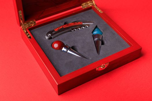 Gift set of corkscrew and removable lids. Wine corks and bottle openers in a wooden box on a red background.
