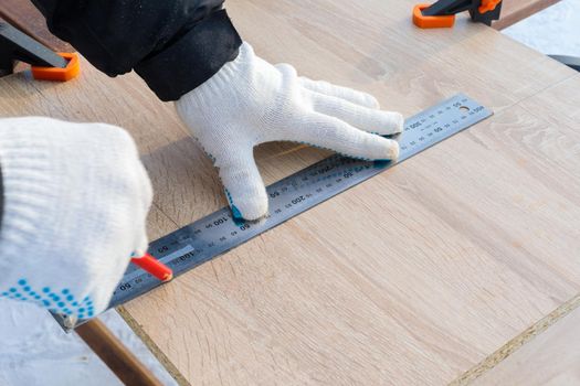 A man, a worker, marks it with a square and a pencil on a chipboard board. Draws a line.