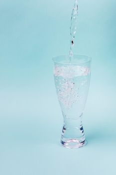 A jet of water fills transparent glass against a blue background. White bubbles rise.