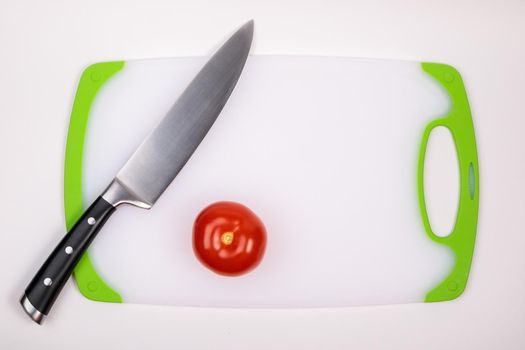 A fresh red tomato and a large chef's knife lie on a cutting board. On an isolated white background.