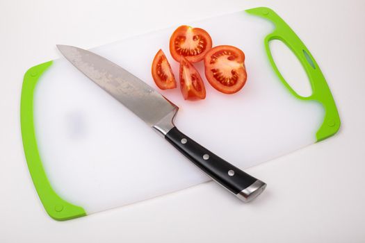 On a cutting board is a fresh red cut tomato and a large chef's knife. On an isolated white background.