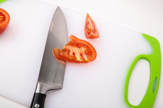 On a cutting board is a fresh red cut tomato and a large chef's knife. On an isolated white background.