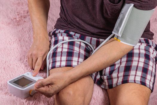 A 50-year-old man measures his blood pressure with a blood pressure monitor at home, sitting on his bed in his home clothes. Surprised by the instrument readings