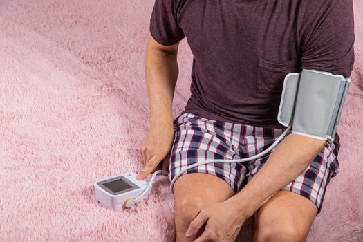 A 50-year-old man measures his blood pressure with a blood pressure monitor at home, sitting on his bed in his home clothes. Surprised by the instrument readings