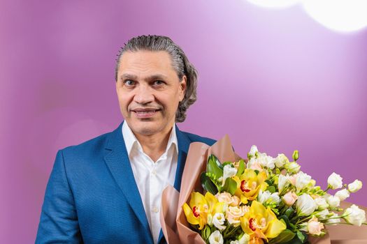 Smiling 50-year-old man in a blue jacket with a bouquet of flowers on a uniform background. Long gray hair