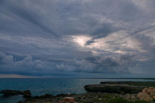A calm sunset on a dark blue sea. Thick clouds on the horizon. In the foreground is a rocky shore. Romantic mood.