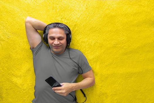 50-year-old man listens to music with headphones at home, lying on the bed. Relaxing, enjoying.