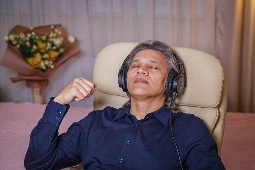 50-year-old man listens to music on headphones at home, sitting in a chair. Relaxing delight.