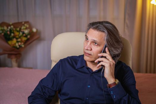 A 50-year-old man with long hair speaks on the phone at home, sitting in a chair. Relaxing delight.