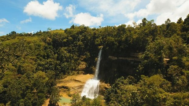 Beautiful waterfall in green forest in jungle. Aerial view:tropical rainforest with waterfall. Waterfall with natural swimming pool in a mountain river canyon. Philippines, Bohol. Travel concept.