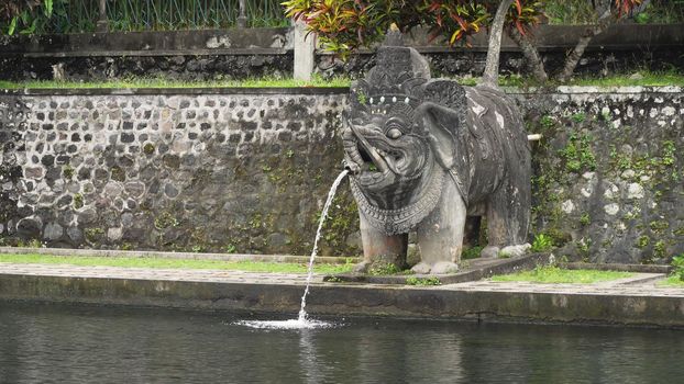 Hindu Balinese Water Palace Tirta Gangga with statues of the gods, fountains in the form of a wild boar on Bali island, Indonesia. Tirta Gangga the former royal water palace is a maze of pools and fountains surrounded by a lush garden and stone carvings and statues.