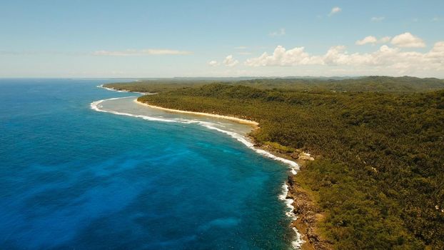 Aerial view: sea and the tropical island with rocks, beach and waves. Coastline of the tropical island Siargao with the mountains and the rainforest on a background of ocean with big waves. Seascape: sky, clouds, ocean. Philippines. Travel concept.