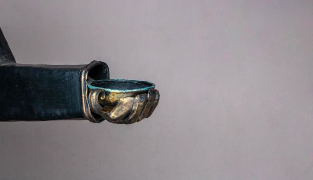 Copper hand with a cup on a beige background under the open sky.