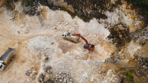 Excavator loads the truck in a limestone quarry. Aerial view wheel loader excavator machine loading dumper truck at quarry. Earth mover loading dumper truck with rocks in quarry. Philippines. Travel concept.