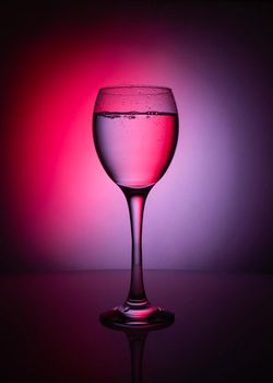 silhouette of transparent glass of whater on red and purple background