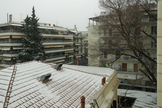 Snow falling on residential area with blocks of flats surrounded be trees.