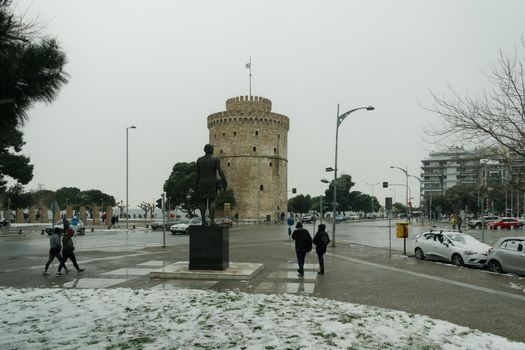 People in warm clothes and covid-19 masks around White Tower landmark with snow falling.