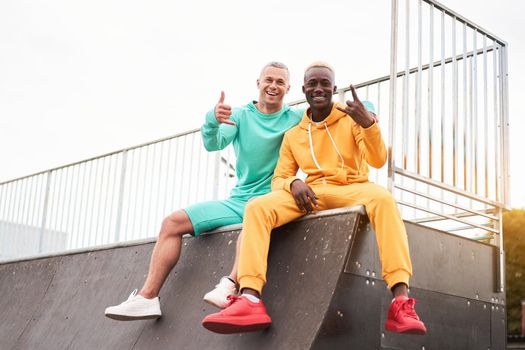 Multi-ethnic friendship Black african-american and caucasian guy friends spending time together on skate park Two multi ethnic student Dressed colorful sportswear.